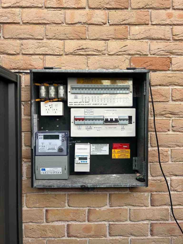 Electrical panel mounted on brick wall with various circuit breakers and switches.