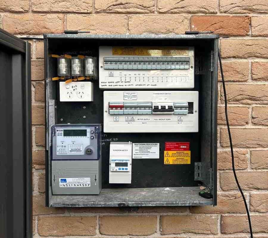 Electrical panel mounted on brick wall with various circuit breakers and switches.