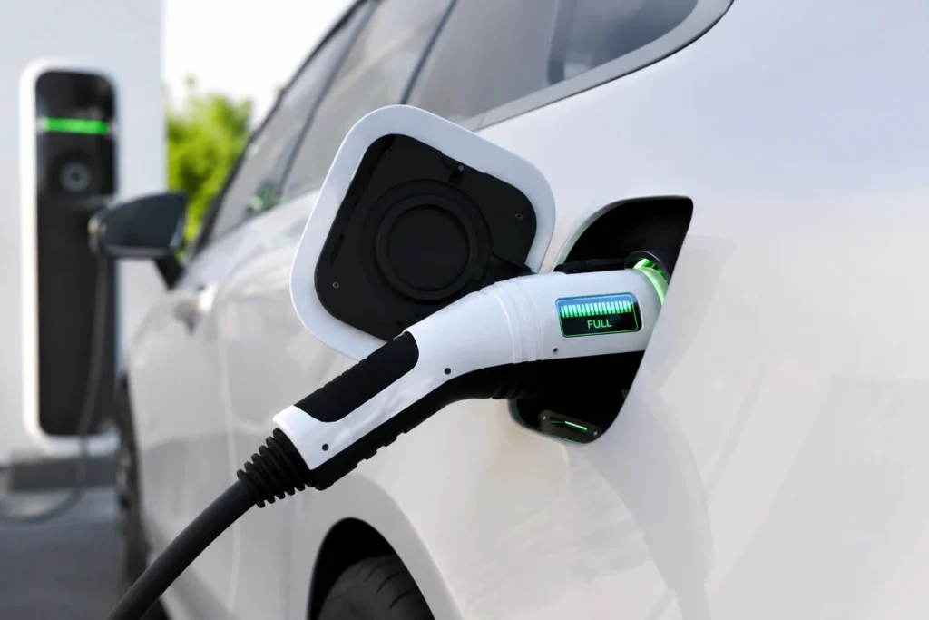 Electric vehicle charging connector plugged into a car at an EV charging station.
